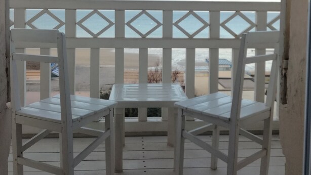 En balkon med et hvidt bord og stole, med udsigt over en strand.