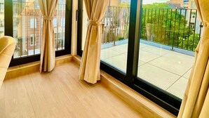Ein Zimmer mit großen Fenstern, Blick auf Gebäude und einem Balkon.