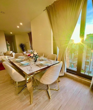 A dining area with a table set for four, a potted plant, and a view of buildings through large windows. - Chic 6-Guest Apartment in Antwerpen (Antwerpen)