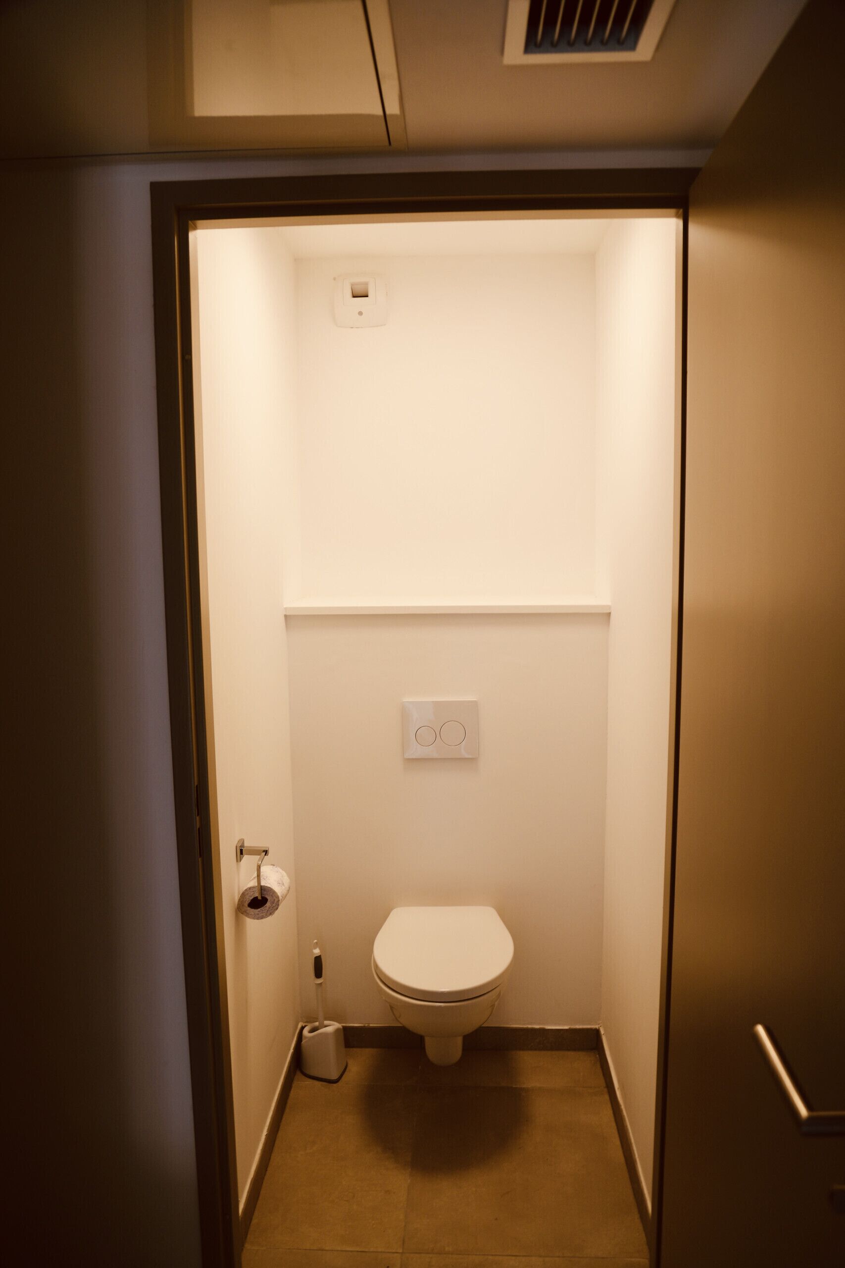 A small, enclosed bathroom with a toilet, a hand dryer, and a toilet paper holder.