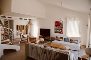 A spacious living area with a staircase, a sofa set, a TV, and a large artwork on the wall. - Luxury duplex overlooking the Etang de Thau (Sète)