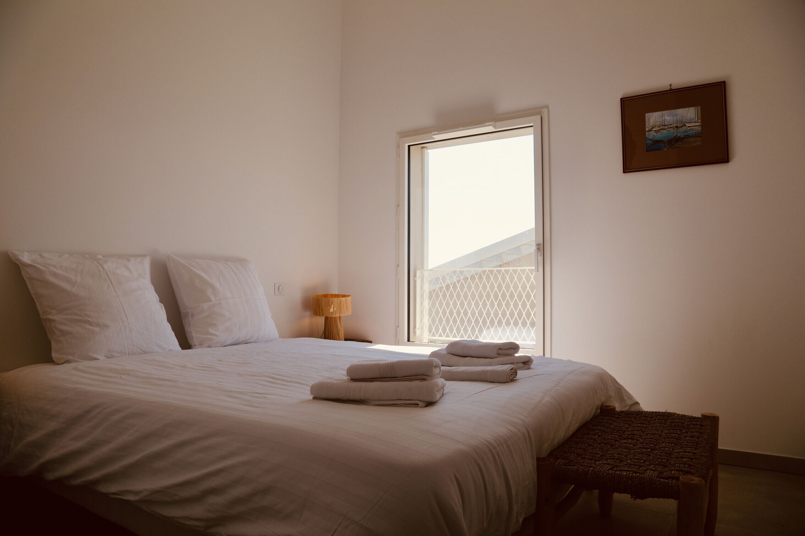A bedroom with a bed, pillows, a bench, a lamp, and a picture on the wall.