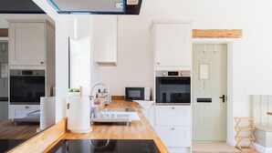 A modern kitchen with white cabinetry, a black countertop, and a wooden floor. - The Annexe of Richmond Barn - Gateway to Cotswolds (Swindon)