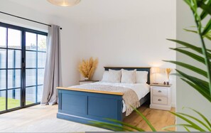 A bedroom with a bed, bedside table, lamp, and a view of the outdoors. - The Annexe of Richmond Barn - Gateway to Cotswolds (Swindon)