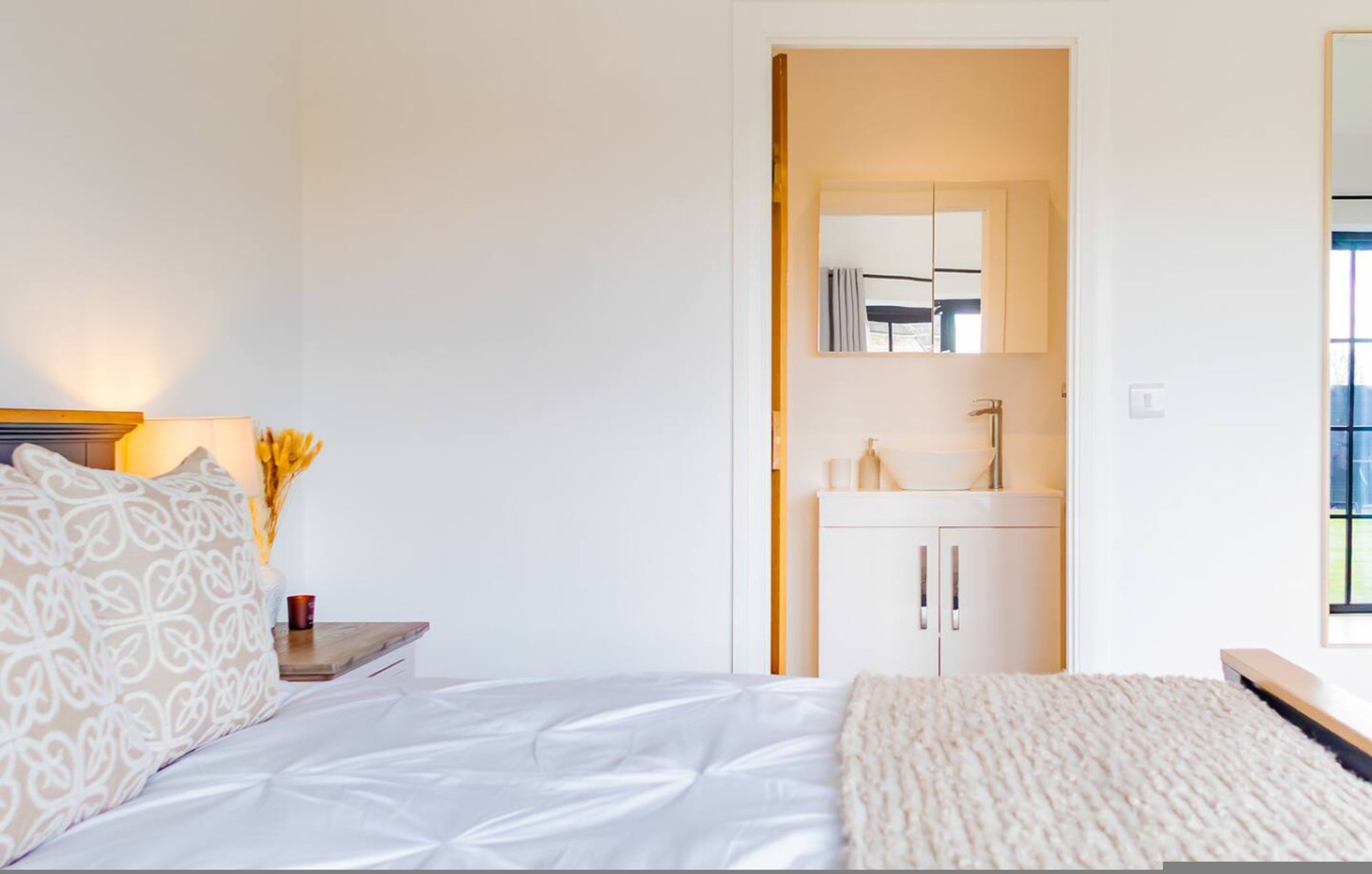A bedroom with a bed, bedside table, lamp, and a view of the bathroom.