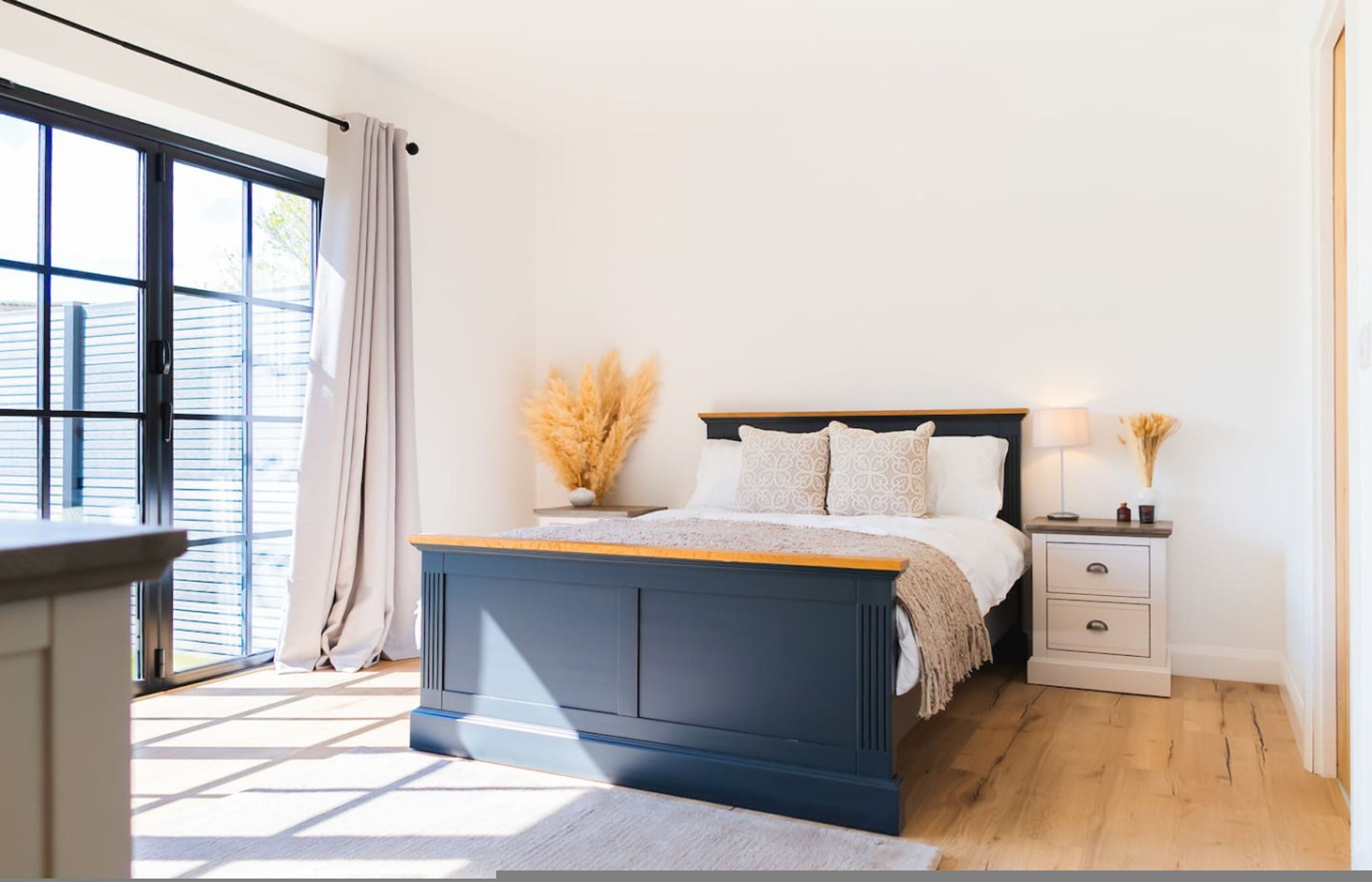 Ein Schlafzimmer mit Bett, Nachttischen, Vorhängen am Fenster und Blick nach draußen.