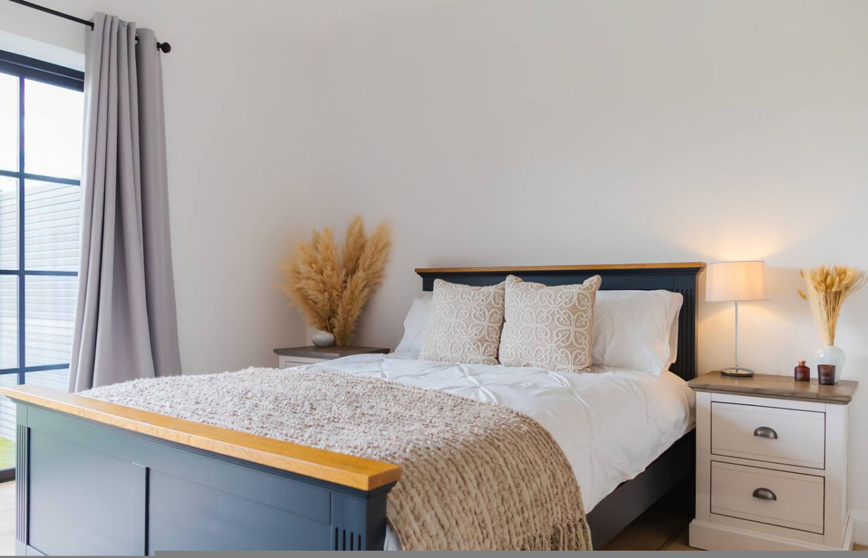 Une chambre moderne avec un lit, des tables de chevet, une commode et une fenêtre avec des rideaux.