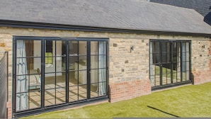 A stone building with large sliding glass doors, a brick exterior, and a sloped roof. - The Annexe of Richmond Barn - Gateway to Cotswolds (Swindon)