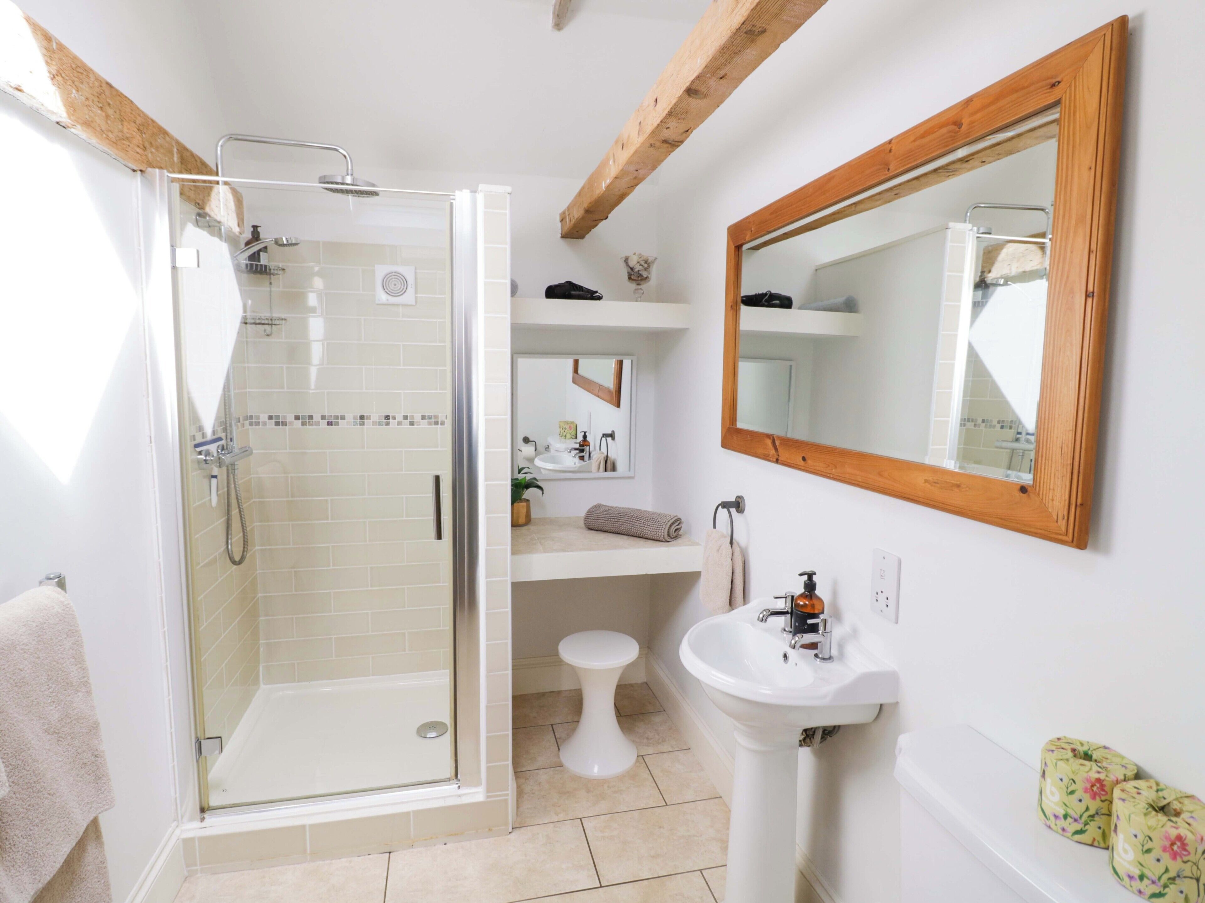 A bathroom with a glass-enclosed shower, a pedestal sink, and a wooden-framed mirror.
