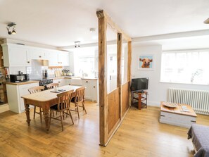 A kitchen with white cabinets, a wooden dining table, and a TV on a stand. - Hallidays Cottages - The Cottage (Oakham)