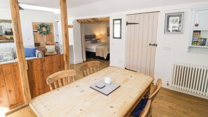 Una mesa de comedor de madera con sillas, una zona de cocina con refrigerador y un dormitorio con cama y ventana.