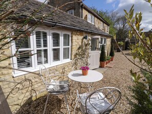 A stone house with a gravel patio, a round table, two metal chairs, and potted plants. - Hallidays Cottages - The Cottage (Oakham)