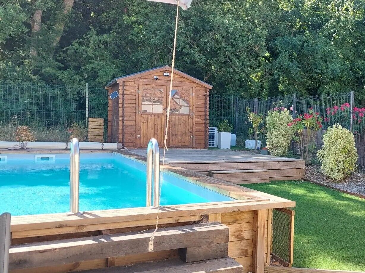 A wooden deck with a swimming pool, a wooden cabin, and a fenced garden area.