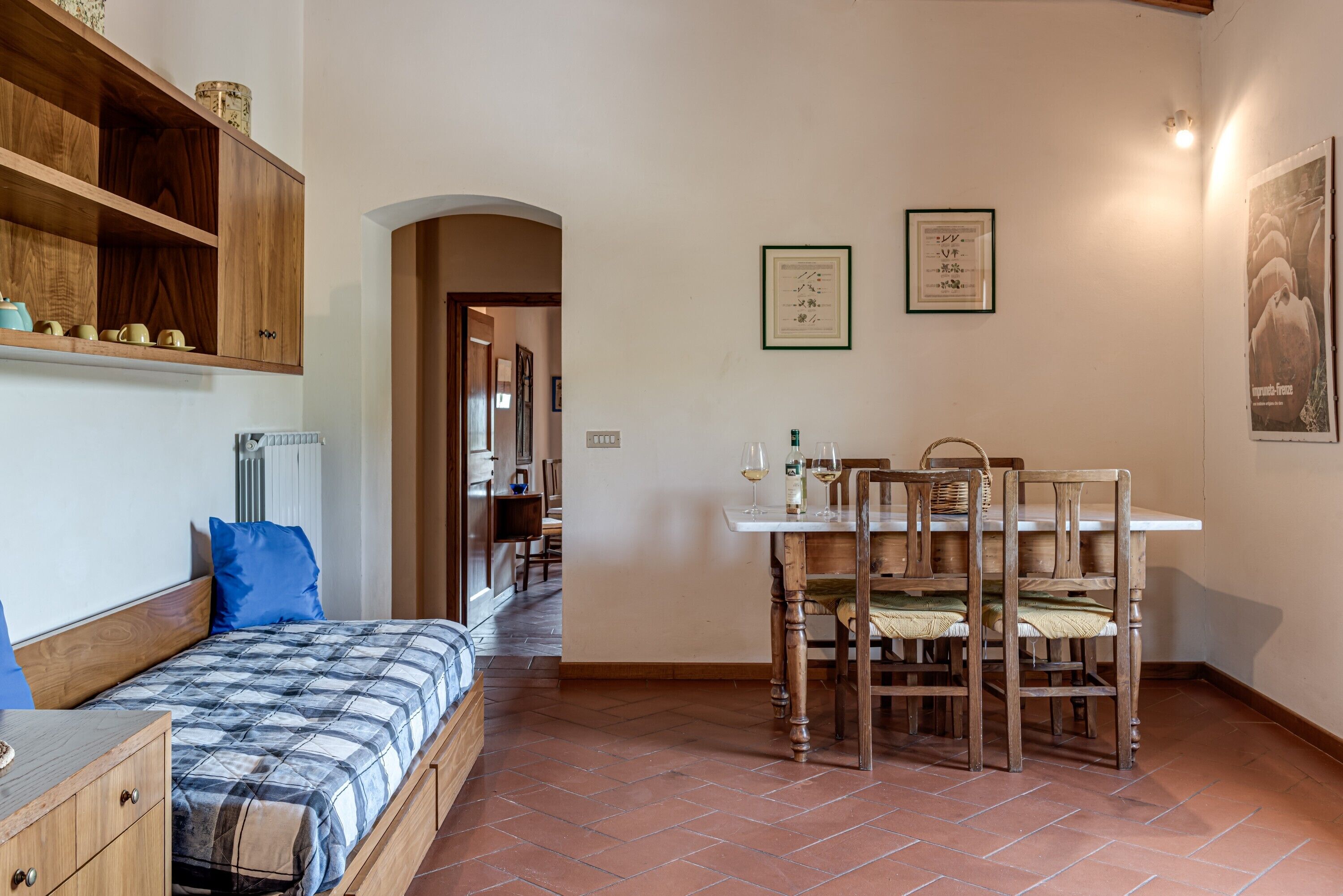 Um quarto com uma cama, um armário de madeira, uma mesa de jantar com cadeiras e um chão ladrilhado.