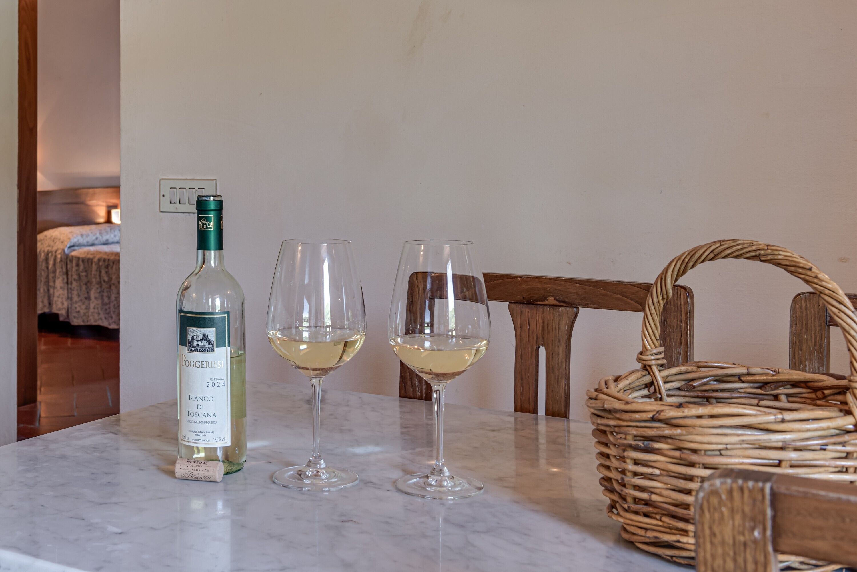 Een fles wijn, twee glazen en een rieten mandje op een marmeren tafel.