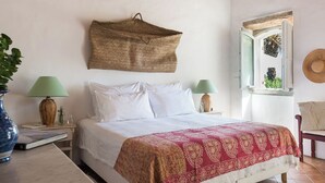 Een slaapkamer met een bed, twee nachtkastjes, een hangmand, een raam met uitzicht en een stoel.