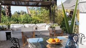 Een terras met een glazen tafel, een schaal mandarijnen en een blauwe vaas met een plant.