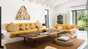Een woonkamer met een houten salontafel, twee banken met kussens, een groene kast en een groot raam.