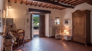 Una stanza con soffitto in legno, termosifone, un armadio, una sedia, un tavolo e una porta che dà sull'esterno.