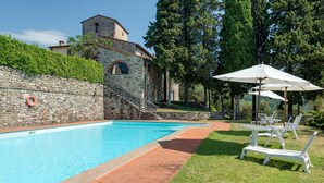 Una piscina con un muro in pietra, una scala in pietra e un edificio con una torre sullo sfondo.