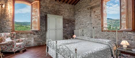 Une chambre rustique aux murs de pierre, avec un lit, une chaise et une armoire.