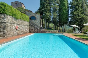 Ein Schwimmbecken mit Steinwänden, einem Rettungsring und einem Steinhaus im Hintergrund.