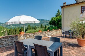 Eine Terrasse im Freien mit Tisch und Stühlen, einem weißen Sonnenschirm und einer Steinmauer.