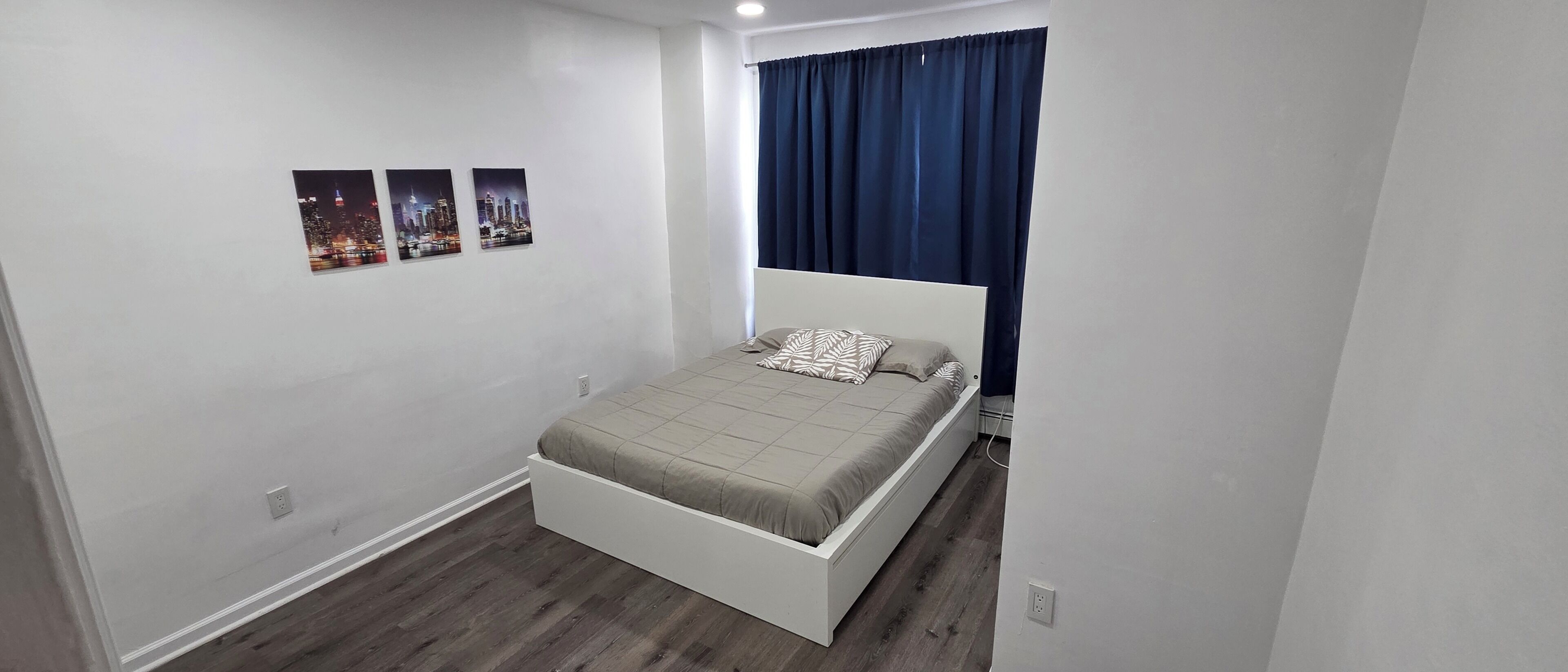 A bedroom with a bed, a window with curtains, and three cityscape pictures on the wall.