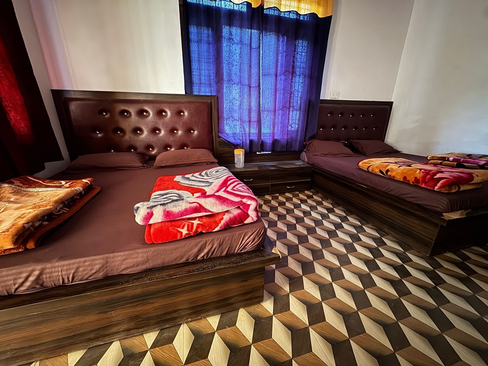 A hotel room with two beds, a patterned floor, and a window with curtains.