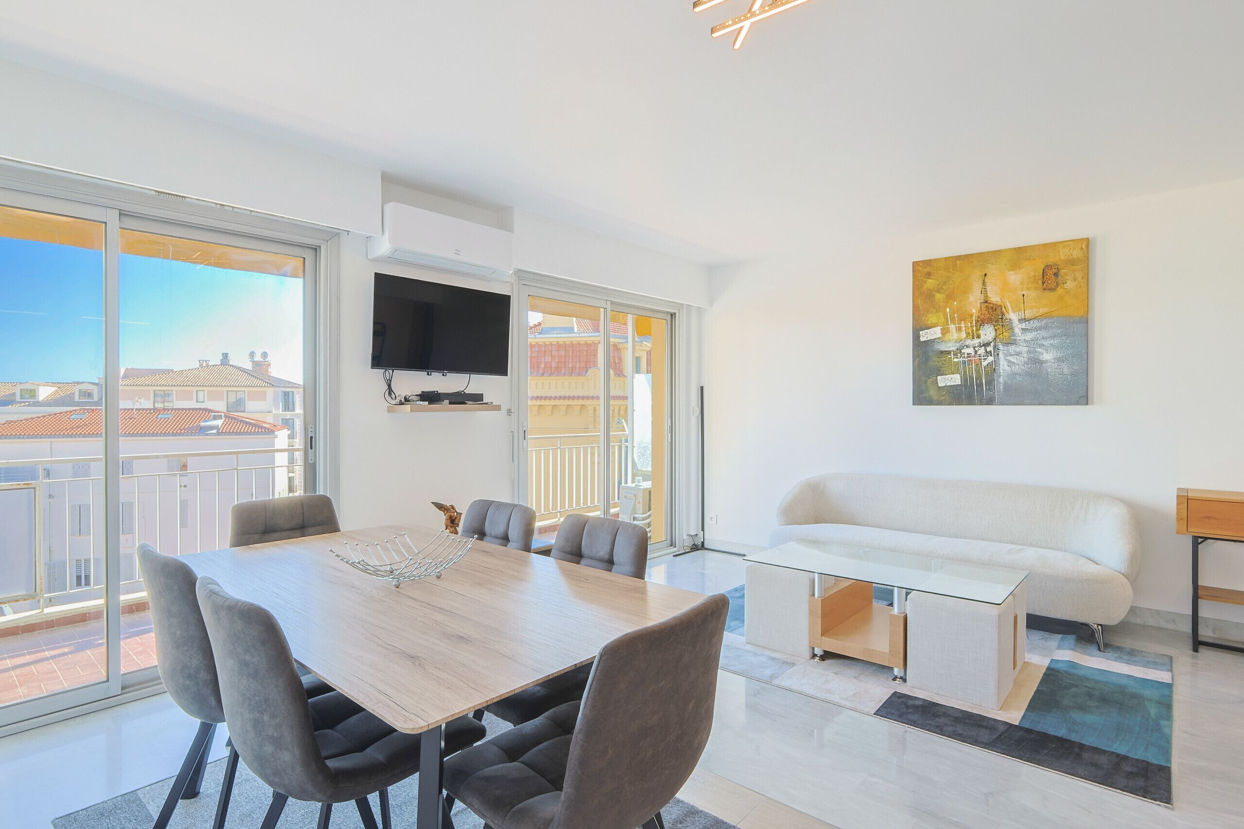 A modern living room with a dining table, sofa, and artwork on the wall.
