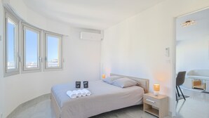Ein modernes Schlafzimmer mit Bett, Nachttischen, einem Sessel und Blick durch große Fenster.