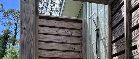 Une structure de douche extérieure en bois, avec des marches menant à la douche, une pomme de douche en métal et un mur en bois.