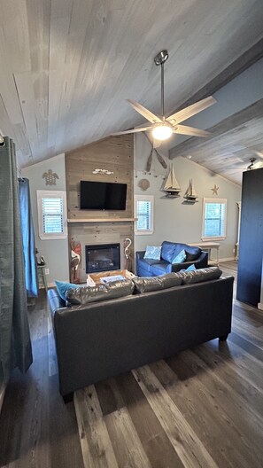 A living room with a sofa, a ceiling fan, a fireplace, and a mounted television.