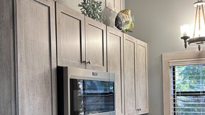 Een keuken met houten kasten, een ingebouwde magnetron, een fornuis en een raam met jaloezieën.