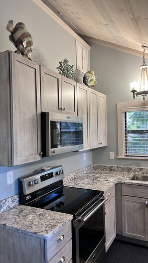 A kitchen with wooden cabinets, a built-in microwave, a stove, and a window with blinds.