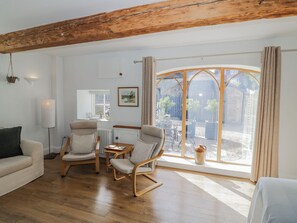 A room with wooden flooring, a sofa, two armchairs, a small table, a radiator, a window with curtains, and a view of the outside. - Hallidays Cottages - The Folly (Oakham)