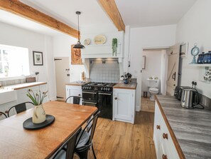 A kitchen with wooden beams, a stove, a sink, and a dining table with chairs. - Hallidays Cottages - The Folly (Oakham)