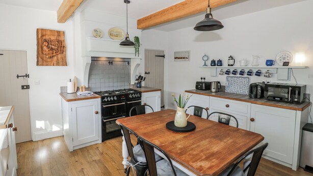A kitchen with white cabinets, a wooden dining table, and a hanging light fixture. - Hallidays Cottages - The Folly (Oakham)