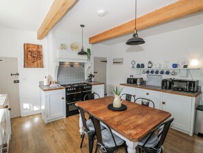 A kitchen with white cabinets, a wooden dining table, and a hanging light fixture. - Hallidays Cottages - The Folly (Oakham)