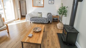 A cozy living room with a sofa, a wooden coffee table, a fireplace, and a large mirror on the wall. - Hallidays Cottages - The Folly (Oakham)