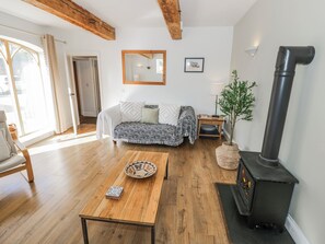 A cozy living room with a sofa, a wooden coffee table, a fireplace, and a large mirror on the wall. - Hallidays Cottages - The Folly (Oakham)