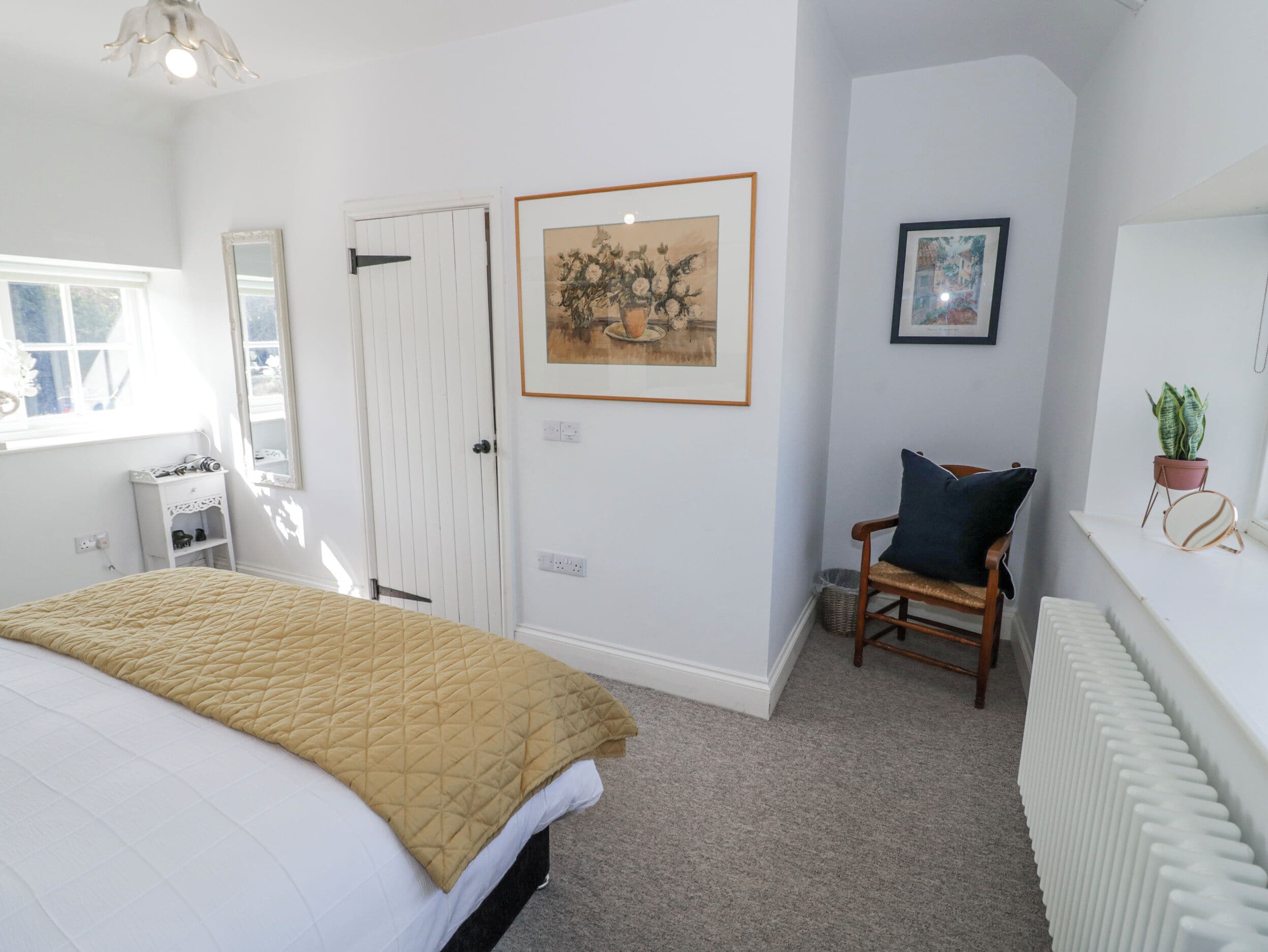 A bedroom with a bed, a chair, a radiator, and two framed pictures on the wall.