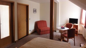 A hotel room with a bed, a red-striped chair, a small table with a TV, and a door.