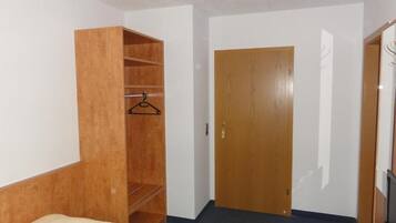 Een kamer met een bed, een houten garderobe, een deur en een bureau met een stoel.