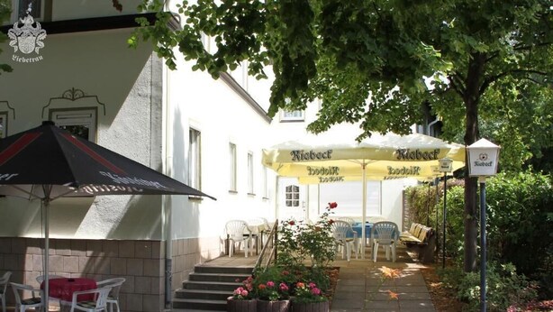A courtyard with outdoor seating, a building with a sign, and a tree providing shade.