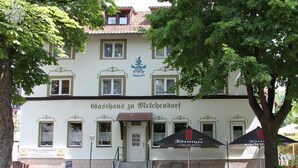 A building with a sign reading 'Gasthof zu Welchendorf' and outdoor umbrellas.