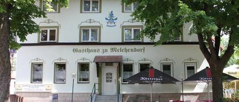 Un edificio con un letrero que dice 'Gasthof zu Welchendorf' y sombrillas exteriores.