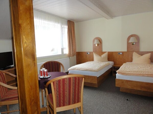 A hotel room with two single beds, a television, a dining table with chairs, and a window with curtains. - Hotel Garni zu Melchendorf (Erfurt)
