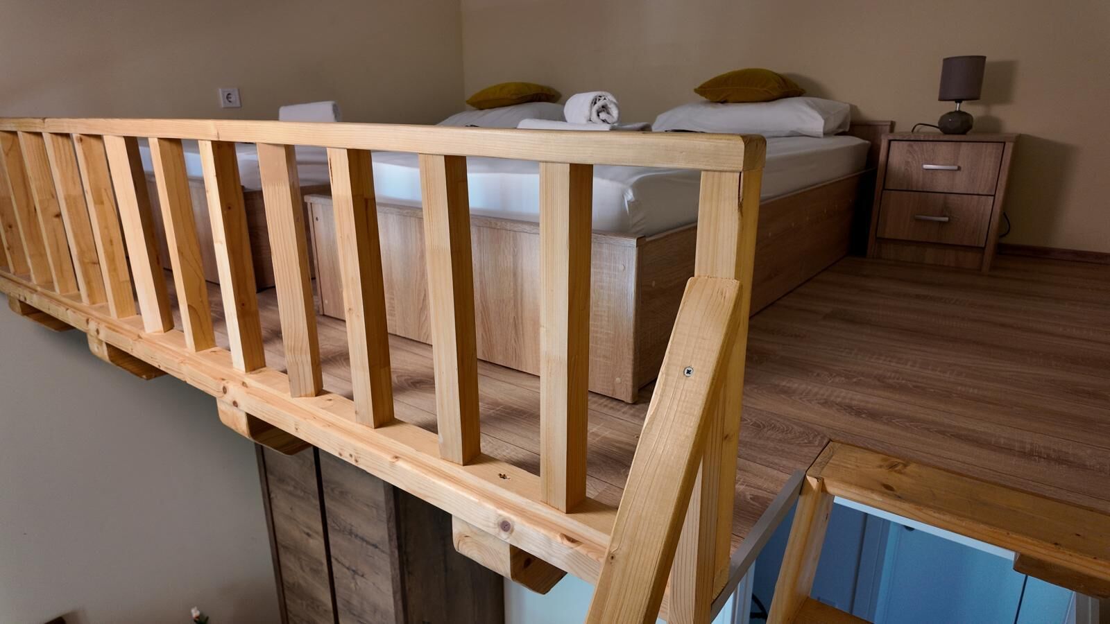 A room with a loft bed, a wooden railing, a nightstand, and a lamp.