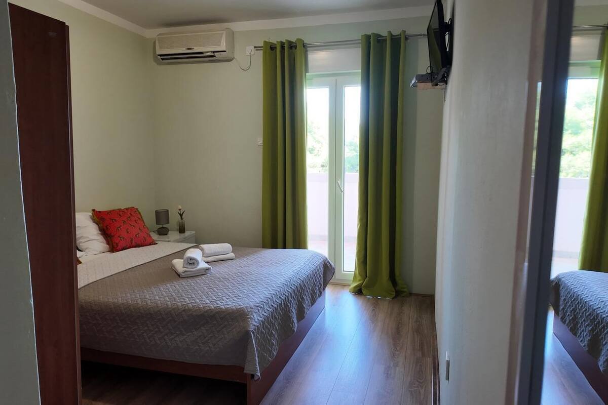 A hotel room with a bed, a nightstand, a TV, and a window with curtains.